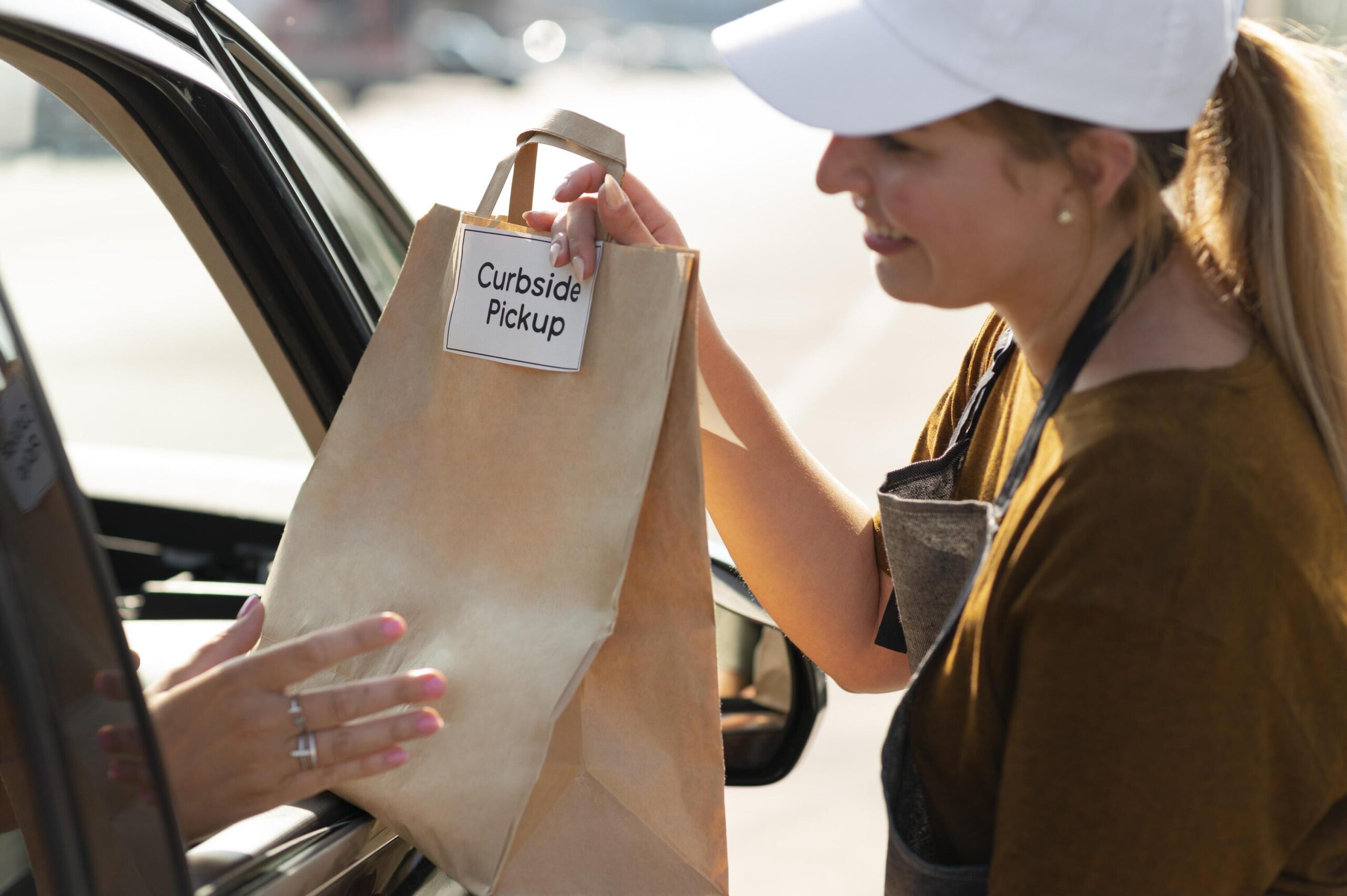 車の窓越しに「Curbside Pickup」と書かれた紙袋を店員から受け取っている様子