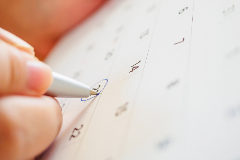 カレンダーの日付にペンで丸をつけ、予定を確定させている手元のクローズアップ